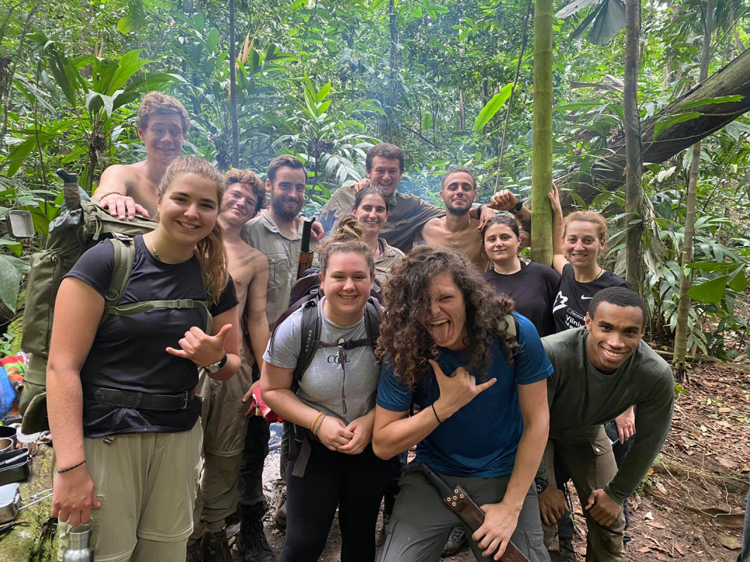 A group of twelve Gapforce participants in front of a fire, in a forest, smiling for a photo.
